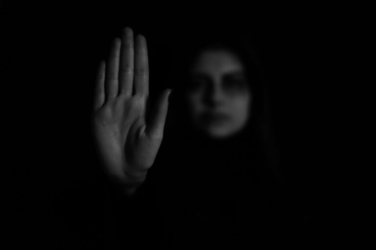 A grayscale photo of a hand showing a stop gesture with a blurred face in the background.