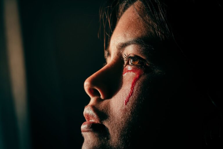 Close-up portrait of a woman with artistic light and red liquid resembling tears, evoking emotion and sorrow.