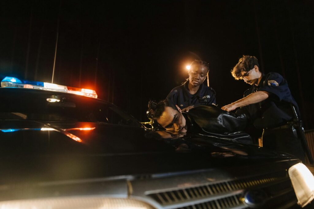 Nighttime arrest scene with police officers detaining suspect by patrol car.