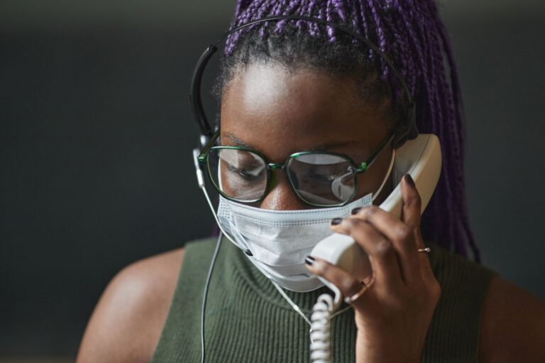 Close-up of a woman wearing a mask and headphones, talking on the phone.