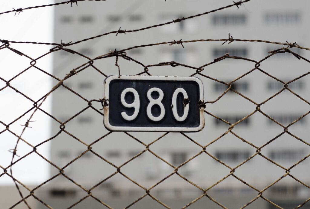 Close-up of a barbed wire fence with a metal number plate. Symbolizes security and restriction.
